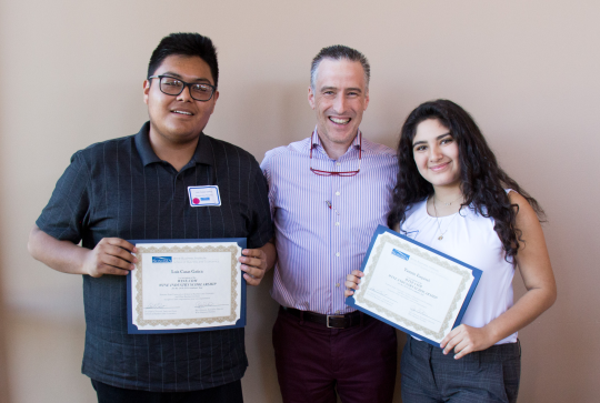 An instructor, flanked by two students showing off their diplomas